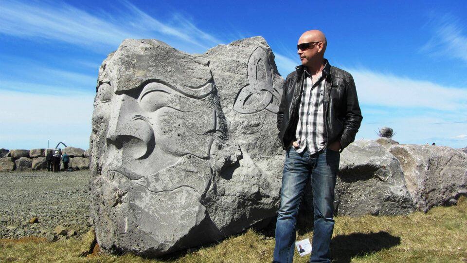 Jón Adólf Steinólfsson standing beside one of his large carved stone sculptures